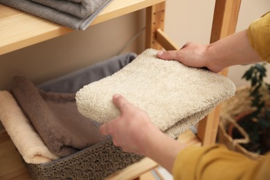 Photo of Woman putting towel into storage basket indoors, closeup