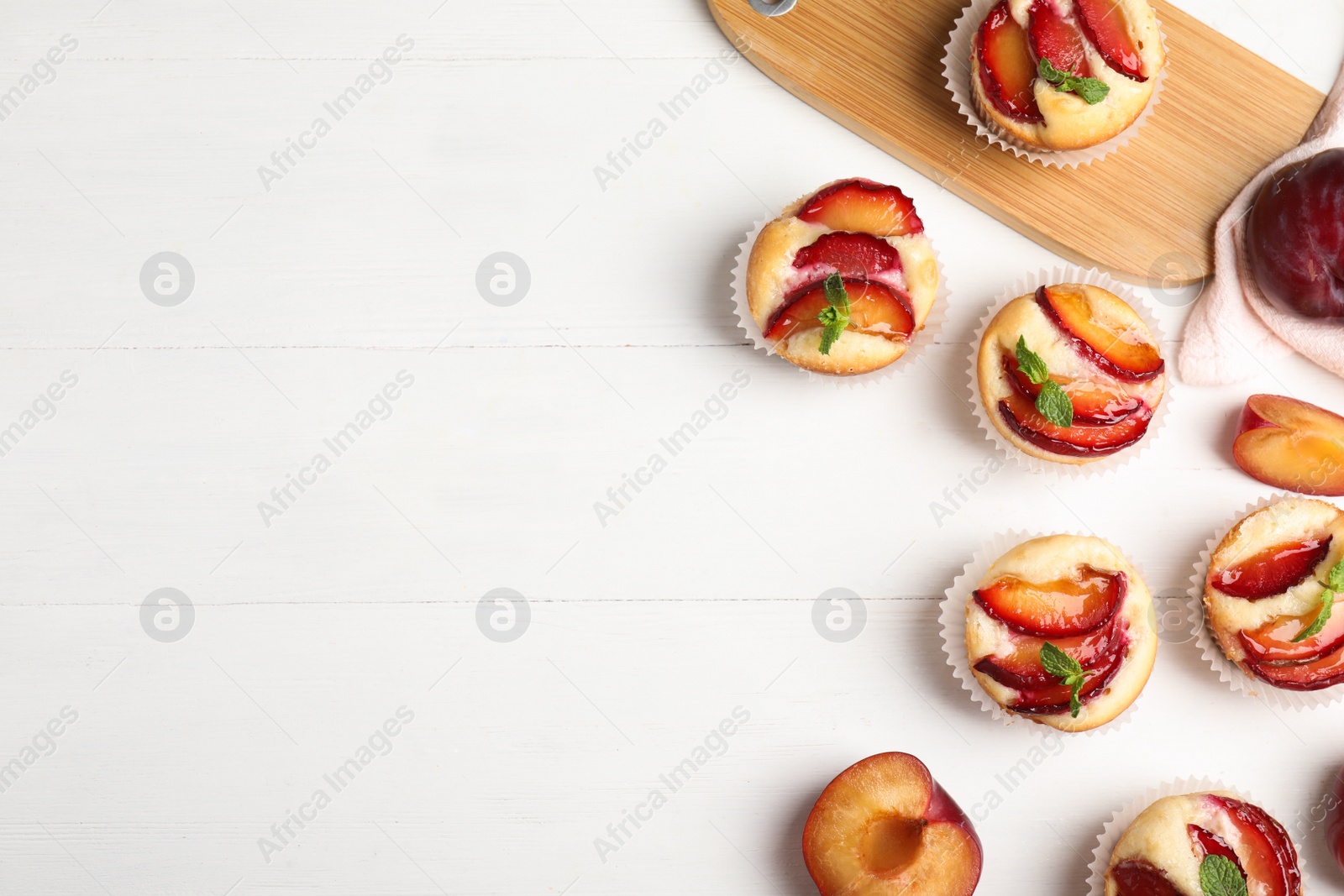 Photo of Delicious cupcakes with plums on white wooden table, flat lay. Space for text