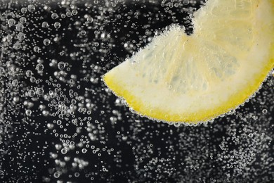 Juicy lemon slice in soda water against black background, closeup. Space for text