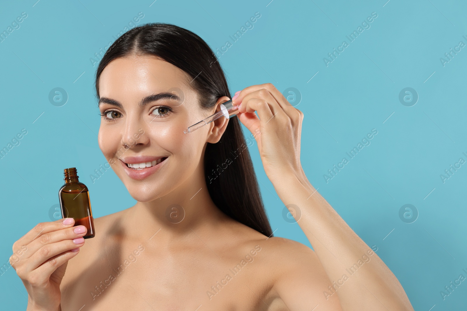 Photo of Beautiful young woman applying serum onto her face on light blue background