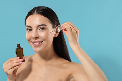 Photo of Beautiful young woman applying serum onto her face on light blue background