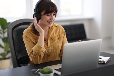 Photo of Woman in headphones watching webinar at table in office