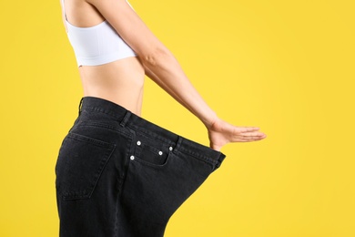 Photo of Young slim woman wearing oversized jeans on yellow background, closeup