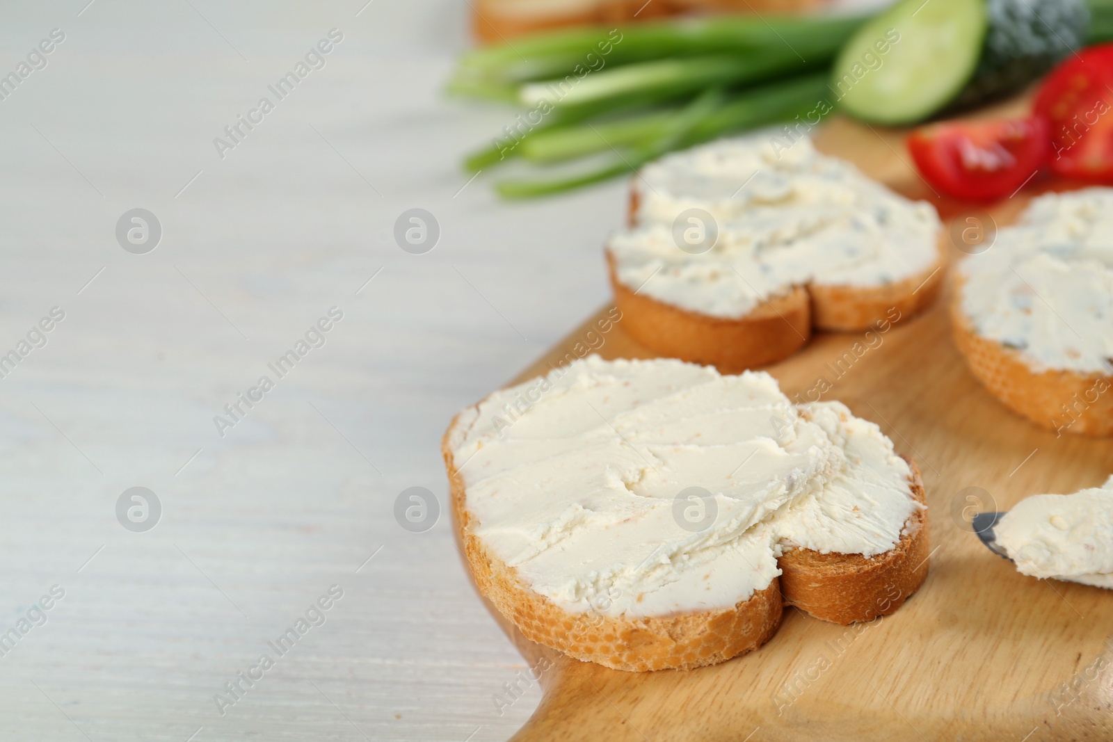 Photo of Toasted bread with cream cheese on white wooden table, closeup. Space for text
