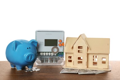 Electricity meter, house model and piggy bank on wooden table against white background