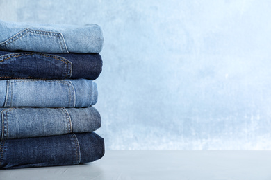 Photo of Stack of different jeans on light table against blue background. Space for text