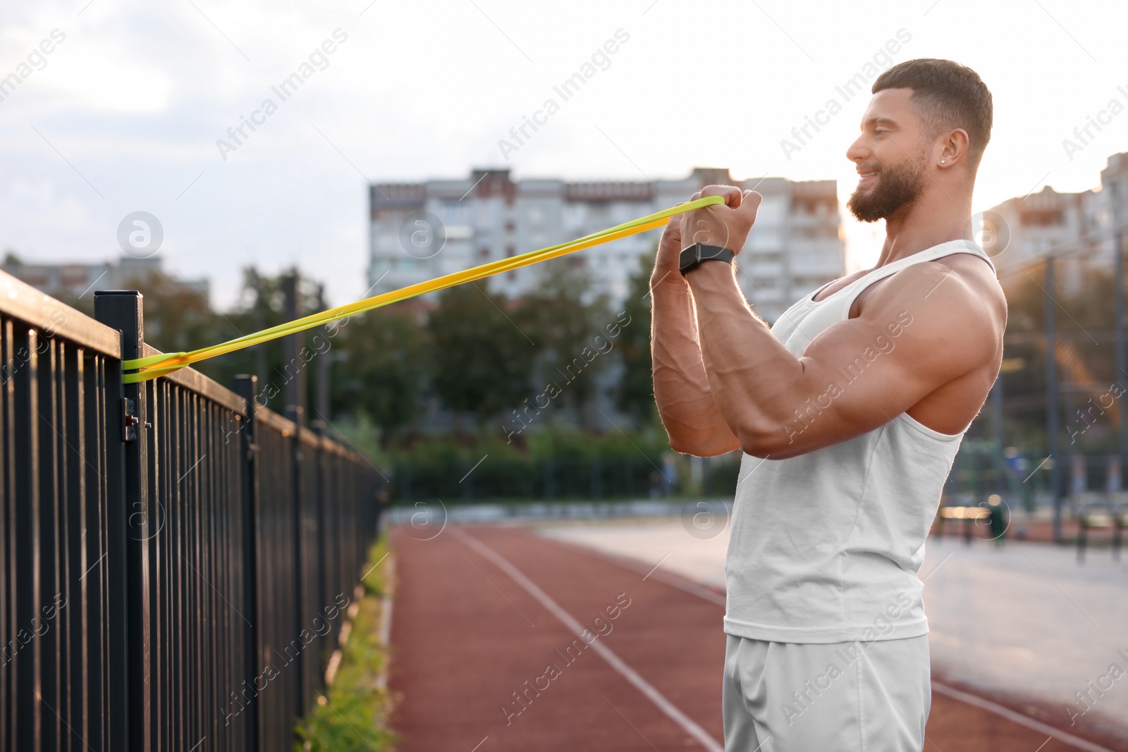 Photo of Muscular man doing exercise with elastic resistance band outdoors