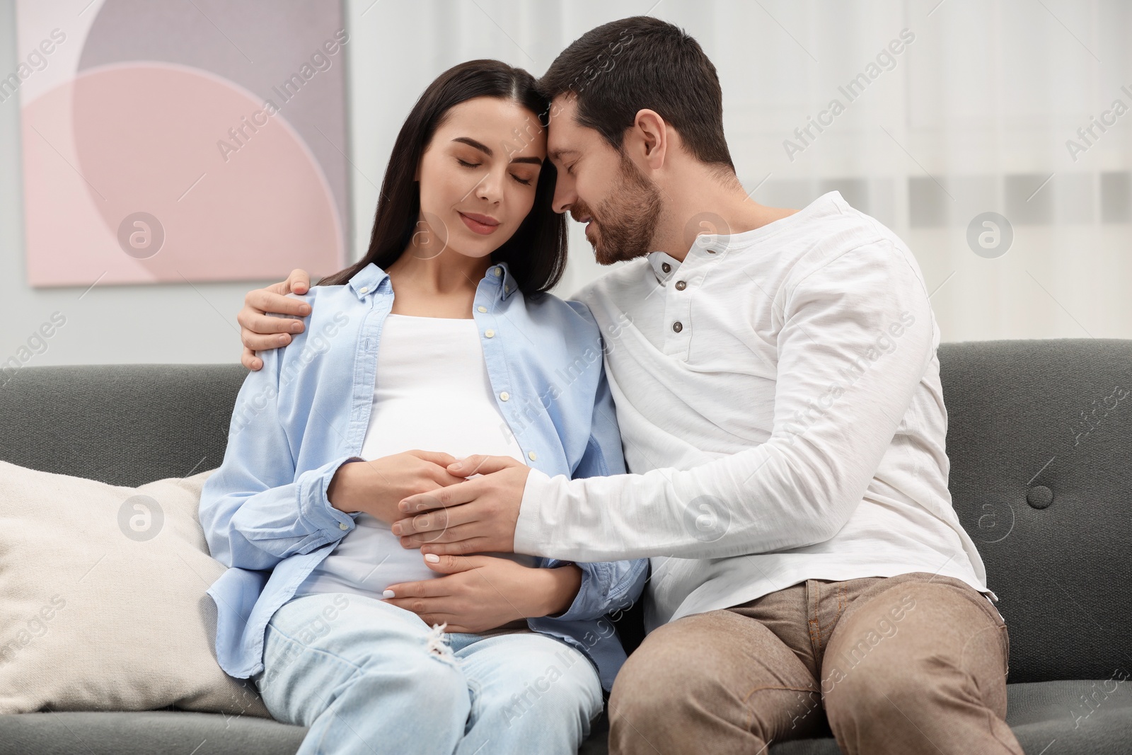 Photo of Pregnant woman with her husband on sofa at home