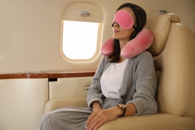 Photo of Young woman with travel pillow and mask sleeping in airplane during flight