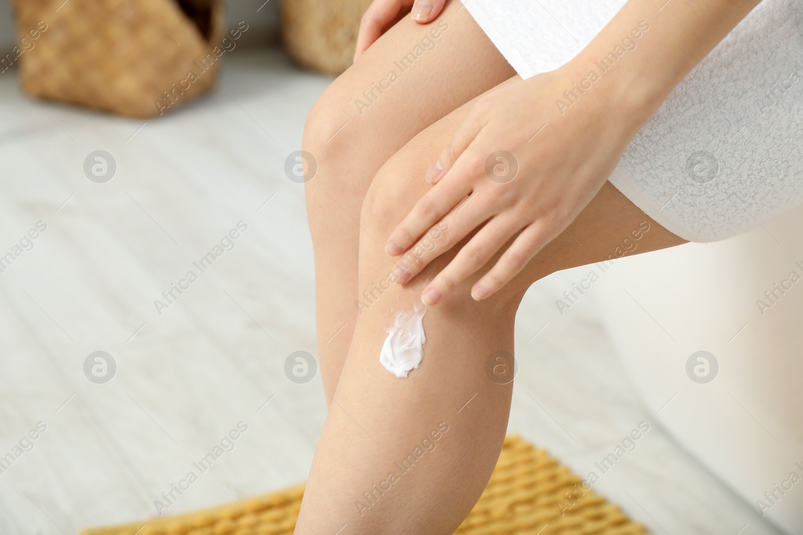 Photo of Young woman applying body cream on leg indoors, closeup