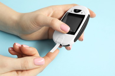 Diabetes. Woman checking blood sugar level with glucometer on light blue background, closeup