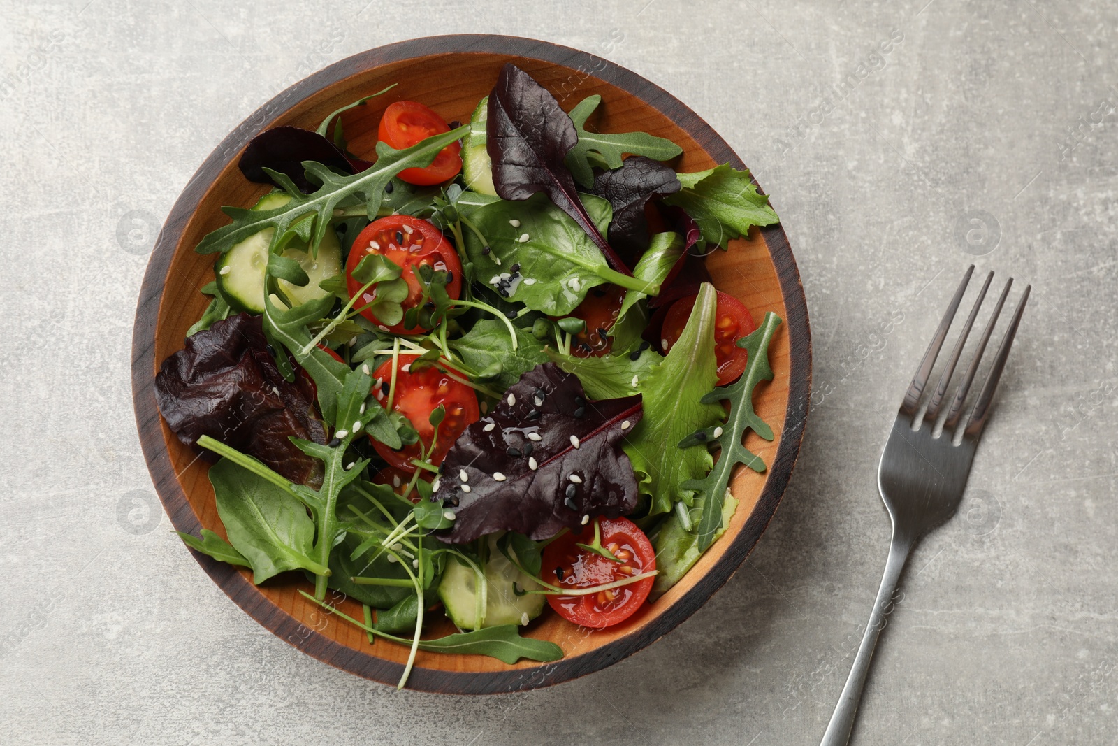 Photo of Tasty fresh vegetarian salad and fork on grey table, top view