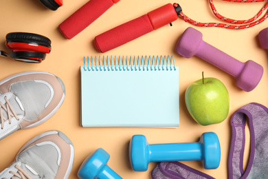 Flat lay composition with fitness equipment, notebook and apple on orange background, space for text