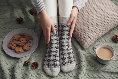 Photo of Woman wearing warm socks on knitted plaid, closeup. Cozy season