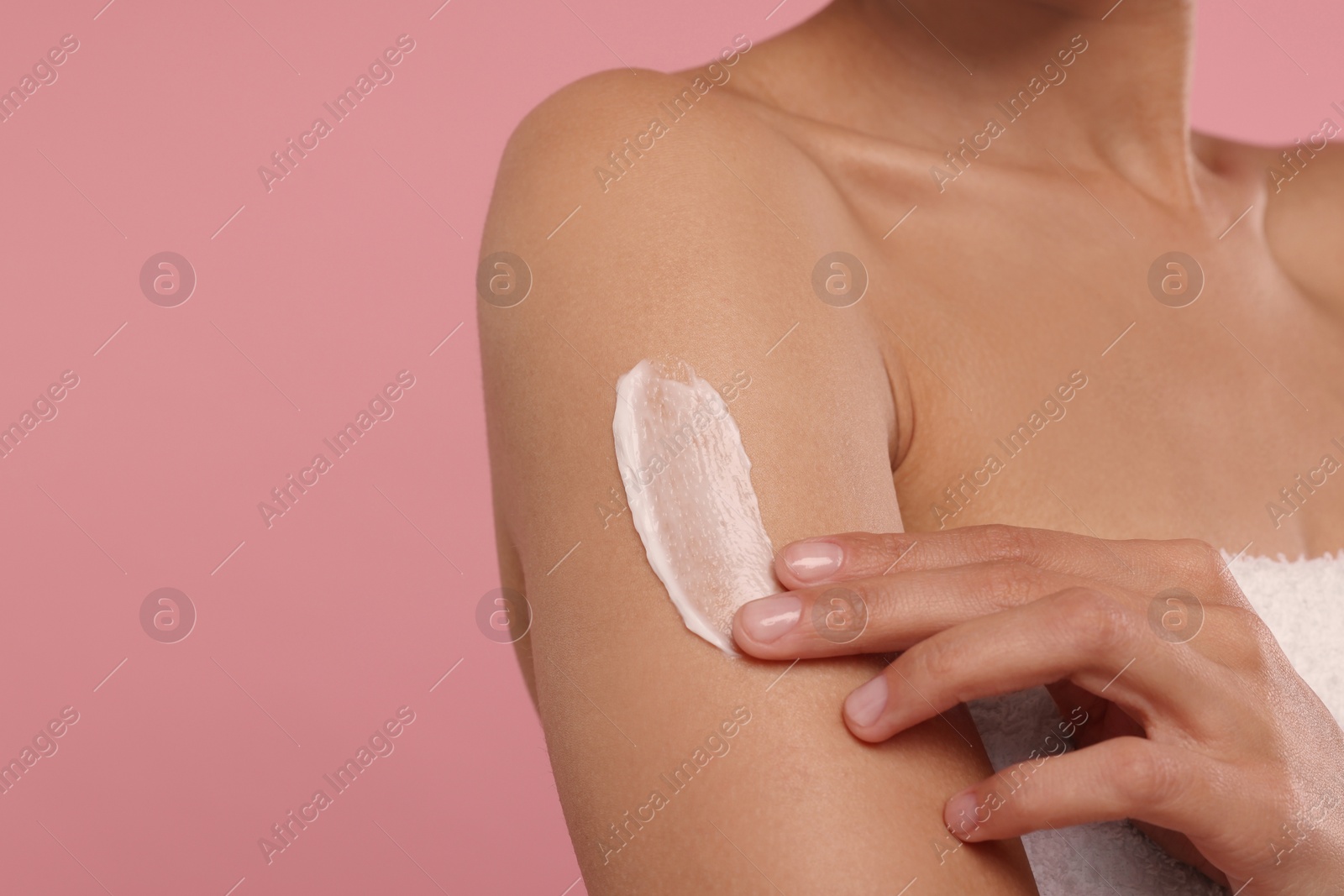 Photo of Young woman applying body cream onto arm on pink background, closeup. Space for text