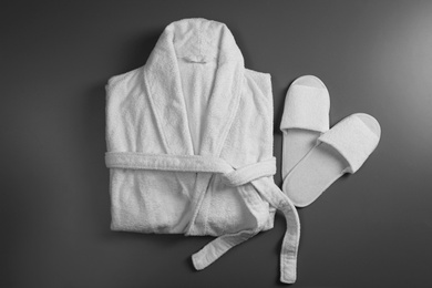 Photo of Clean folded bathrobe and slippers on grey background, flat lay