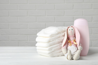Photo of Baby diapers, toy bunny and bottle on wooden table against white brick wall. Space for text