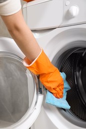 Photo of Woman cleaning washing machine with rag, closeup