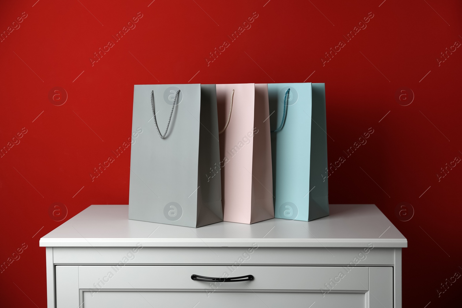 Photo of Paper shopping bags on white chest of drawers against red background