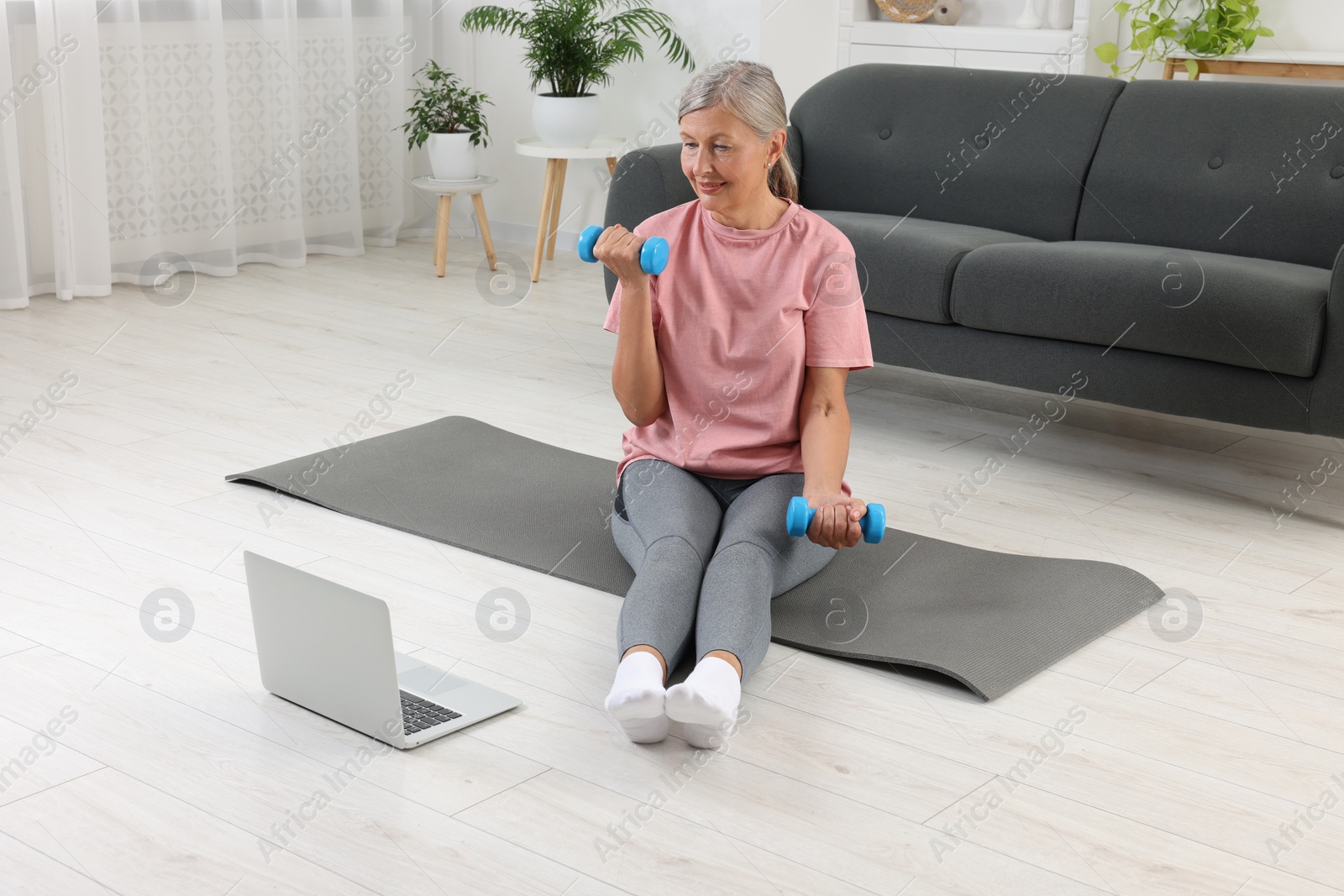 Photo of Senior woman exercising with dumbbells while watching online tutorial at home. Sports equipment