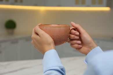 Woman holding elegant pink cup in kitchen, closeup