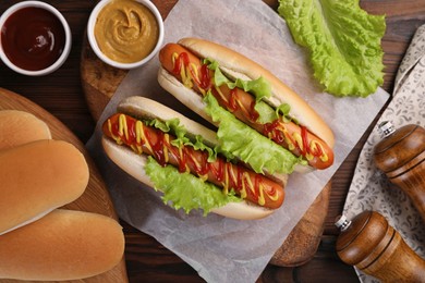 Photo of Tasty hot dogs and ingredients on wooden table, flat lay
