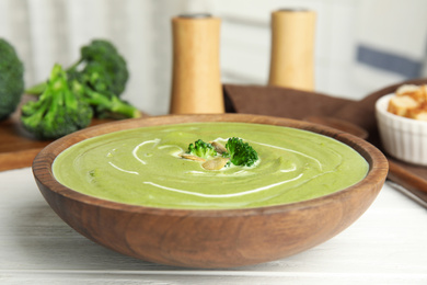 Delicious broccoli cream soup served on white wooden table, closeup