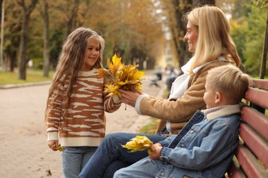 Happy mother and her children spending time together with dry leaves in autumn park