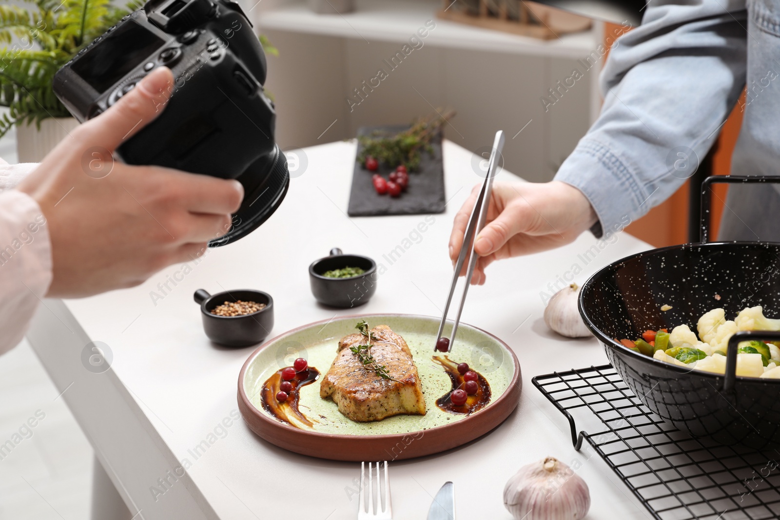 Photo of Professional photographer taking photo while food stylist decorating composition with meat medallion in studio, closeup