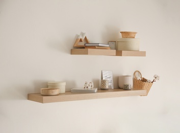 Photo of Wooden shelves with books and different decorative elements on light wall