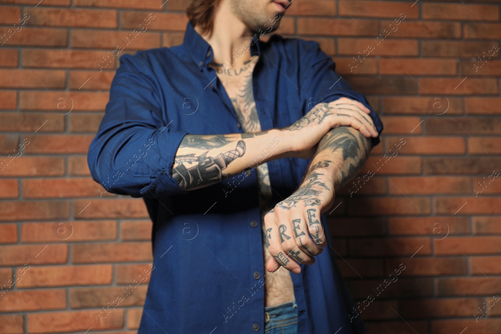 Photo of Young man with tattoos on body near brick wall, closeup