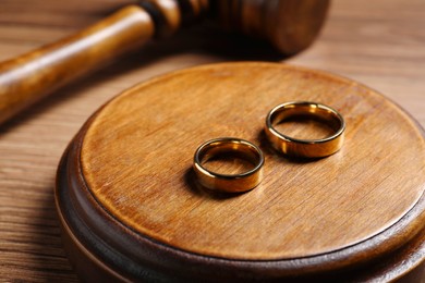 Photo of Divorce process. Wedding rings near gavel on wooden table, closeup