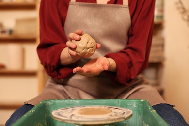 Photo of Woman crafting with clay over potter's wheel indoors, closeup