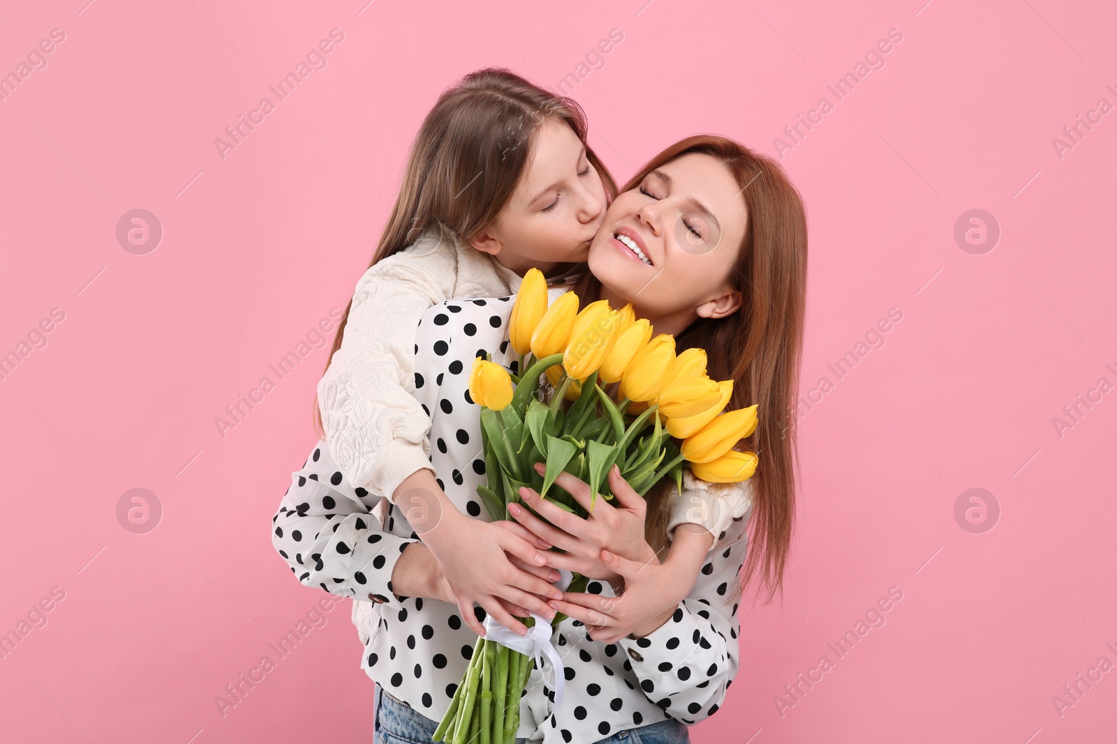 Photo of Mother and her cute daughter with bouquet of yellow tulips on pink background