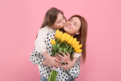 Photo of Mother and her cute daughter with bouquet of yellow tulips on pink background