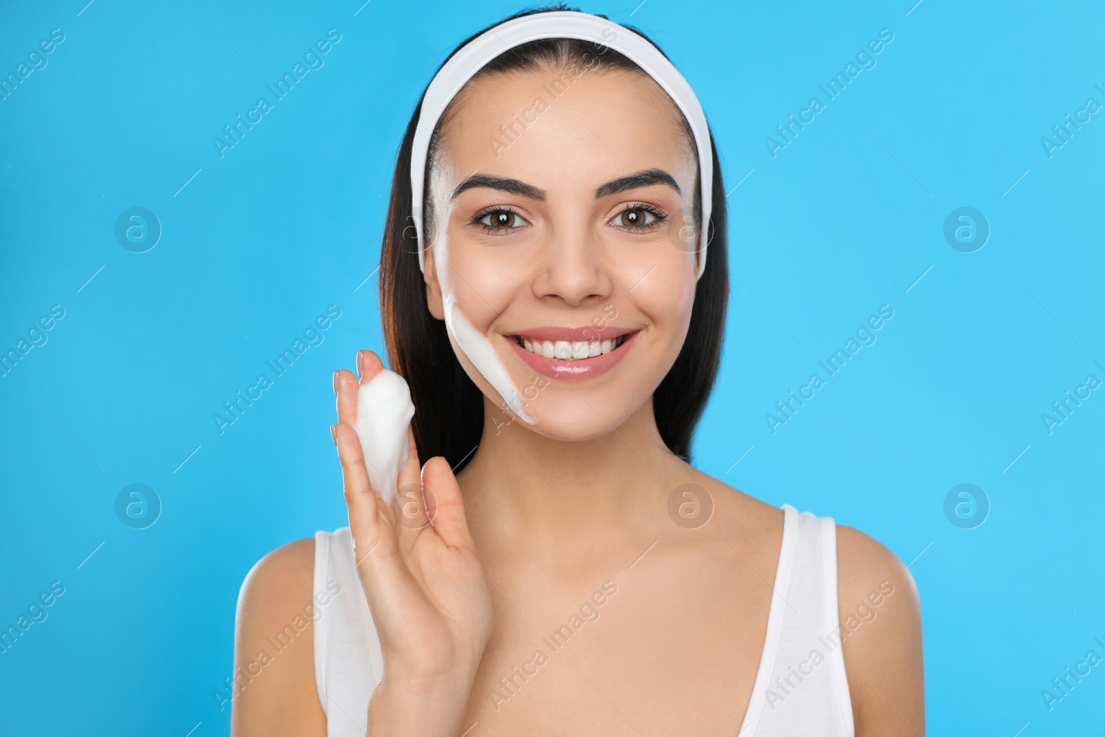 Photo of Young woman applying cosmetic product on light blue background. Washing routine