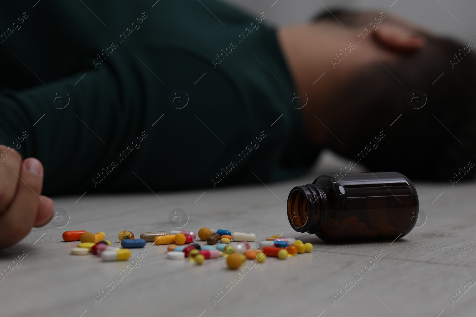 Photo of Man sleeping on floor, focus on overturned bottle with antidepressants