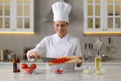 Photo of Professional chef putting cut tomatoes into bowl at white marble table indoors