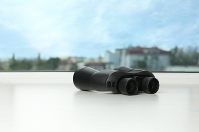Photo of Black binoculars on white window sill. Space for text