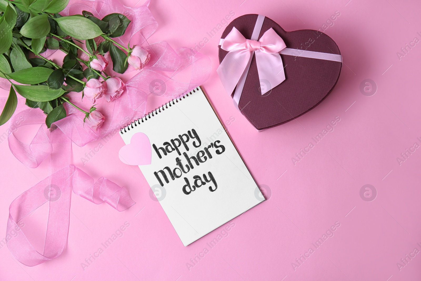 Photo of Notebook with phrase "HAPPY MOTHER'S DAY", flowers and gift box on color background