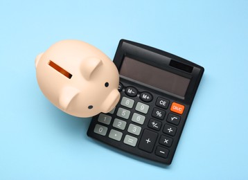 Photo of Calculator and piggy bank on light blue background, top view