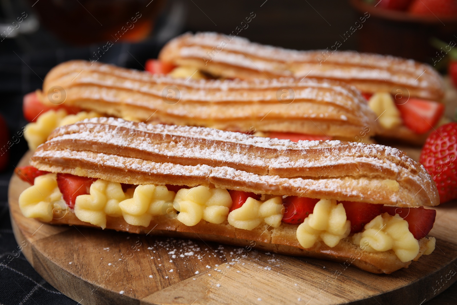 Photo of Delicious eclairs filled with cream and strawberries on table, closeup