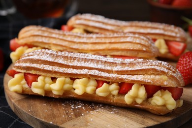 Photo of Delicious eclairs filled with cream and strawberries on table, closeup