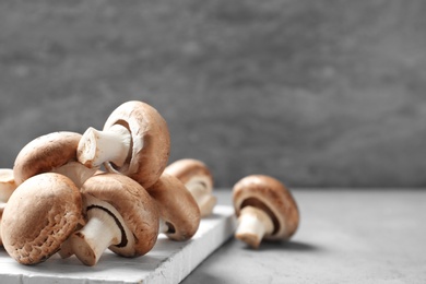 Photo of Fresh champignon mushrooms and wooden cutting board on table, space for text