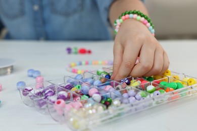 Little girl making beaded jewelry at table, closeup