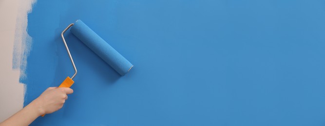 Photo of Woman painting wall with roller, closeup. Redecoration