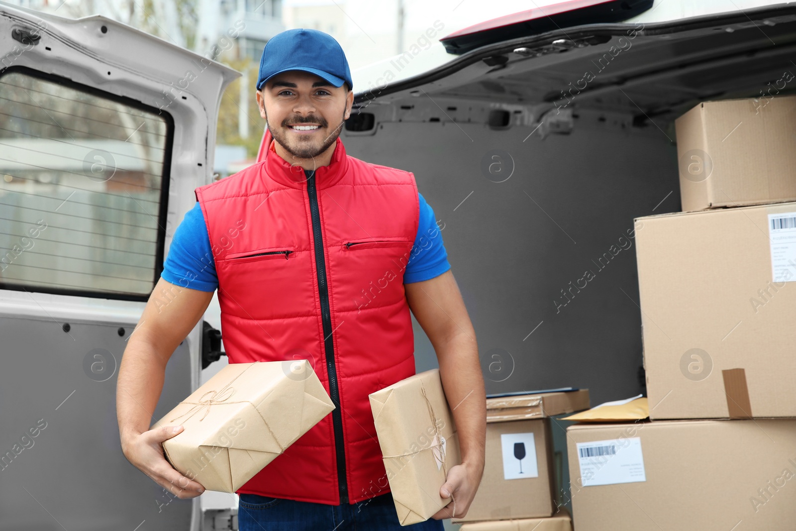 Photo of Young courier with parcels near delivery van outdoors