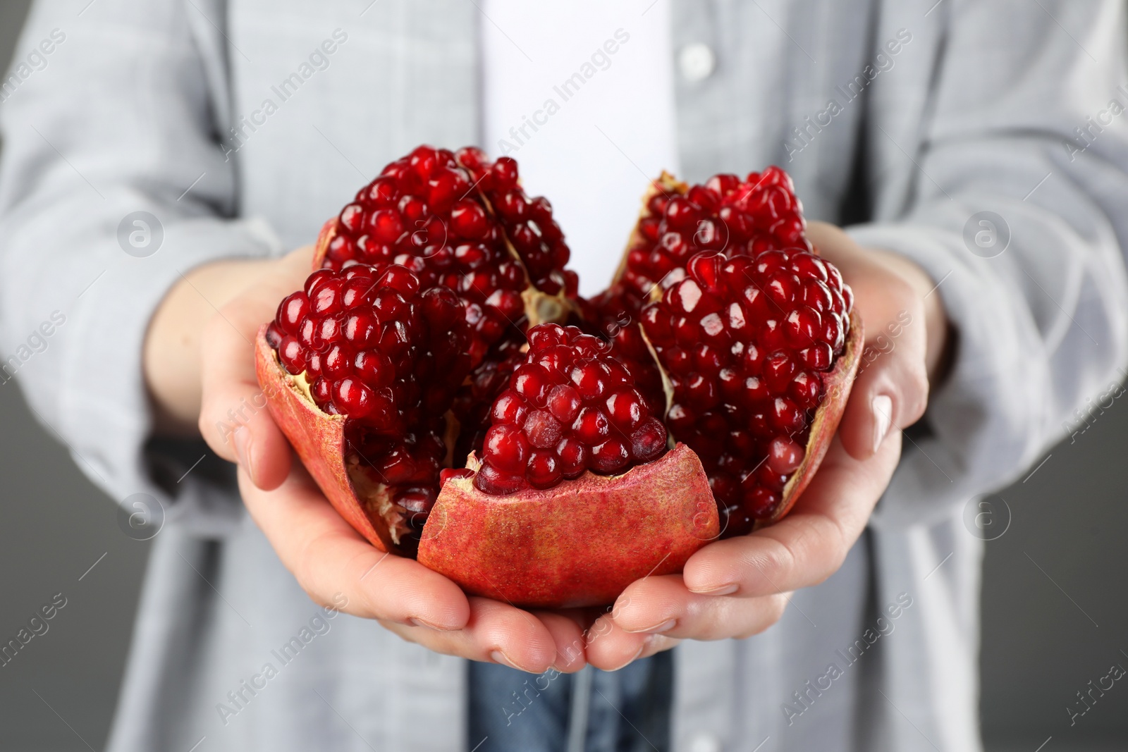 Photo of Woman holding fresh pomegranate on grey background, closeup