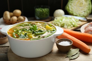 Photo of Saucepan of delicious vegetable soup with chicken, bay leaves and carrots on wooden table