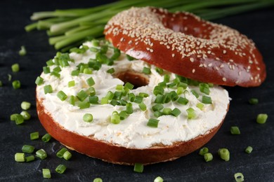 Photo of Delicious bagel with cream cheese and green onion on black table, closeup